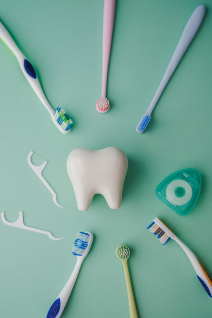 Toothbrushes and dental floss arranged around a large tooth model on a teal background.
