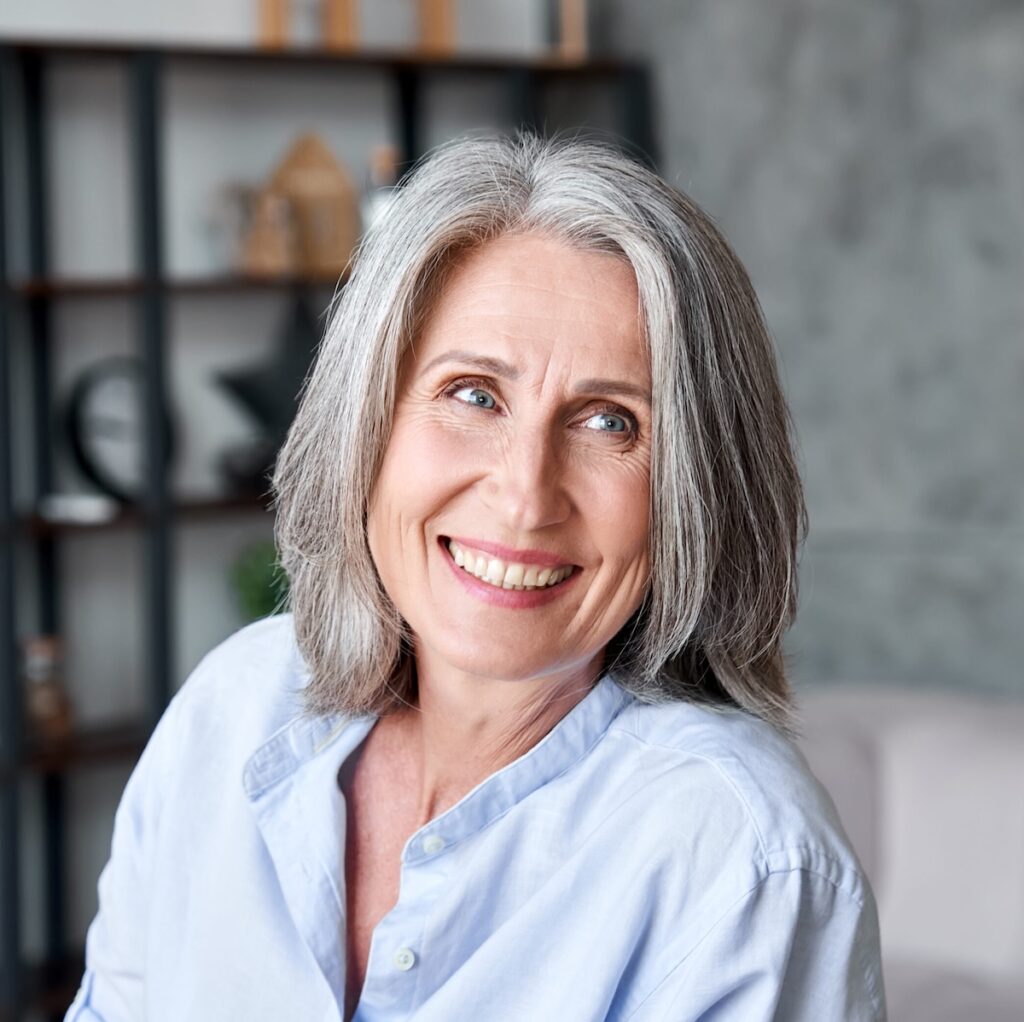Happy beautiful elegant old adult business woman smiling looking away in office. Positive stylish classy grey-haired middle aged mature female teacher, manager, entrepreneur or coach portrait.